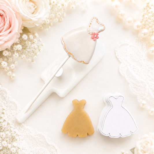 Dress-shaped cake pop cutter and matching cake pop placed on a white stand, styled with a dress cut from cake pop dough