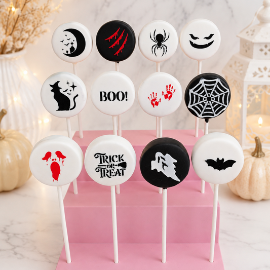 Twelve Halloween-themed round cake pops on white sticks, arranged on a pink display block. The designs include a moon and stars, claw marks, a spider, a smiling face, 'BOO!', red handprints, a spiderweb, a cat, a wolf howl, a bat, and a skull with dripping blood motifs.