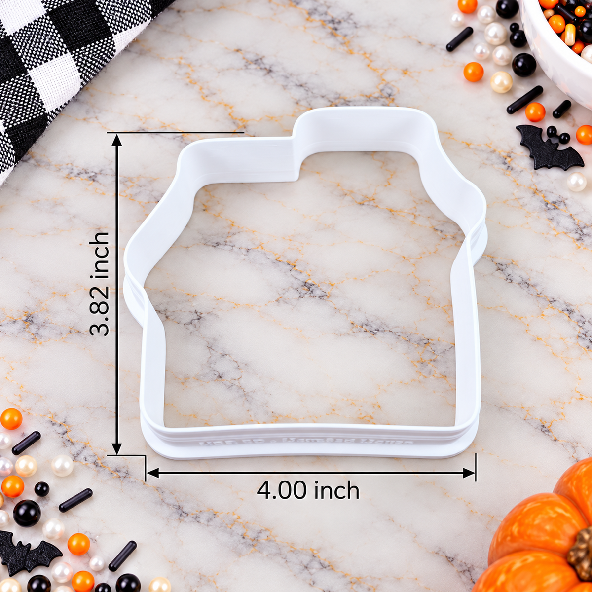 A white cookie cutter shaped like a house, shown on a marble surface with measurement lines and text indicating 3.82 inch height and 4.