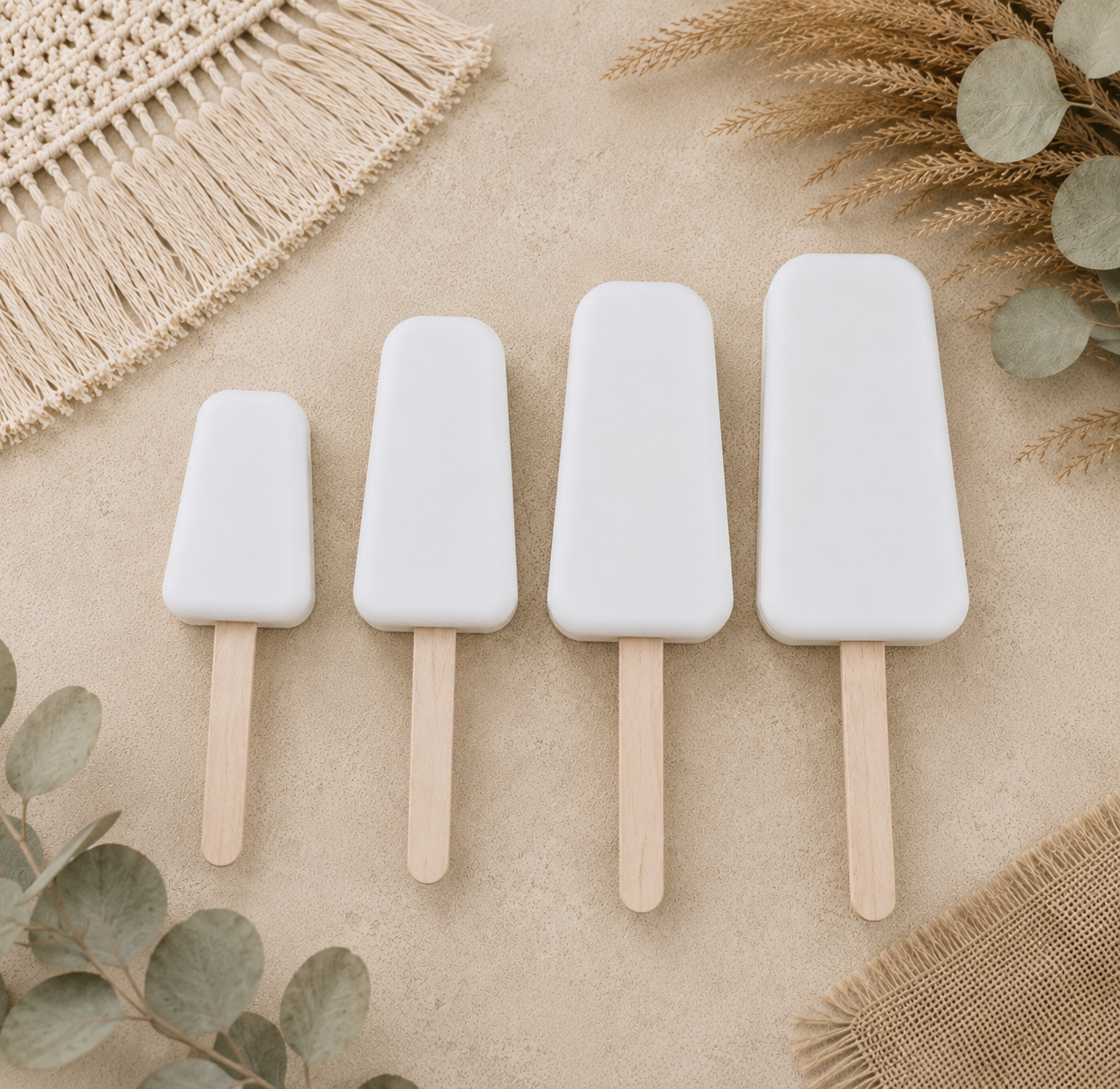 Four white fake cakesicles with wooden sticks arranged in descending size.